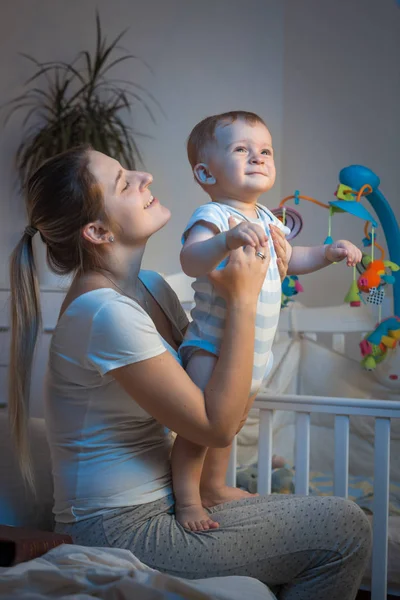 Baby boy sitting on mothers lap in bedroom at night — Stock Photo, Image