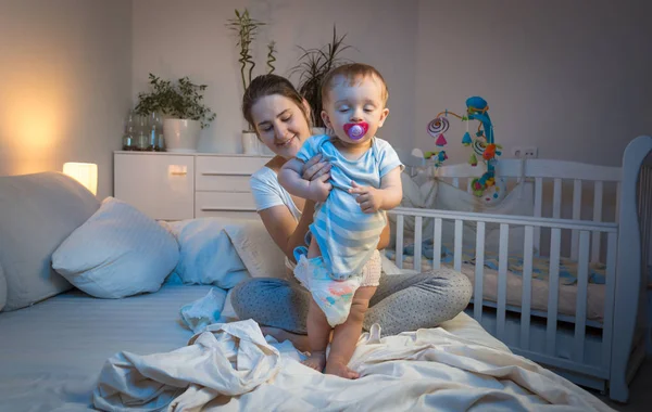 Liebevolle Mutter, die ihrem kleinen Sohn auf dem Bett Windeln wechselt — Stockfoto