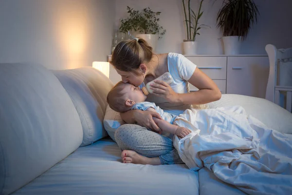 Genç anne bebeğini geceleri yatakta şişe besleme — Stok fotoğraf