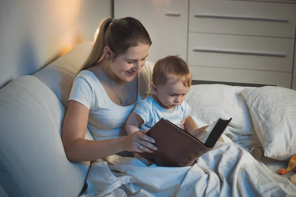 Young mother storytelling to her adorable baby boy at bed — Stock Photo, Image