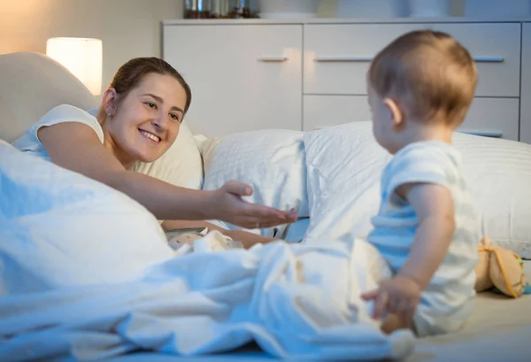 Beautiful smiling woman with baby in bed at night — Stock Photo, Image