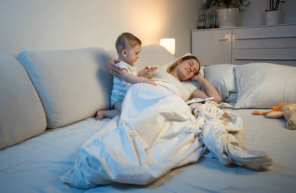 Bebê tentando acordar cansado mãe dormindo na cama — Fotografia de Stock