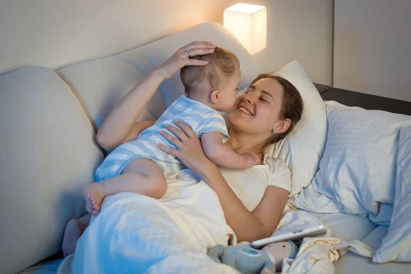 Feliz joven madre jugando y abrazando a su bebé en la cama en —  Fotos de Stock