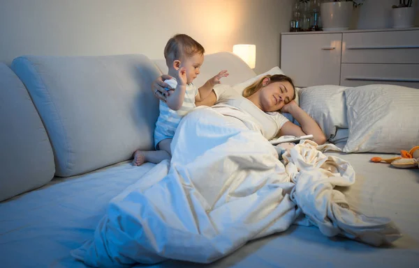 Cansada joven madre tratando de dormir mientras su bebé la despierta —  Fotos de Stock