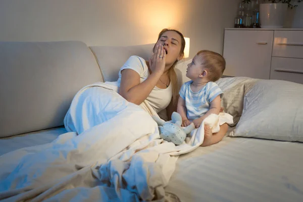 Kisfiú ül ágyas és látszó-on tátongó fáradt anya — Stock Fotó