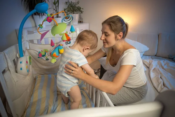 Happy young mother looking at her baby in crib before going to s — Stock Photo, Image