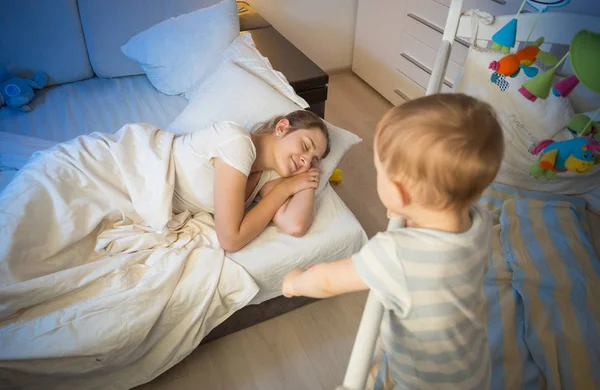 Bebé en cuna tratando de despertar a la madre que se quedó dormida —  Fotos de Stock