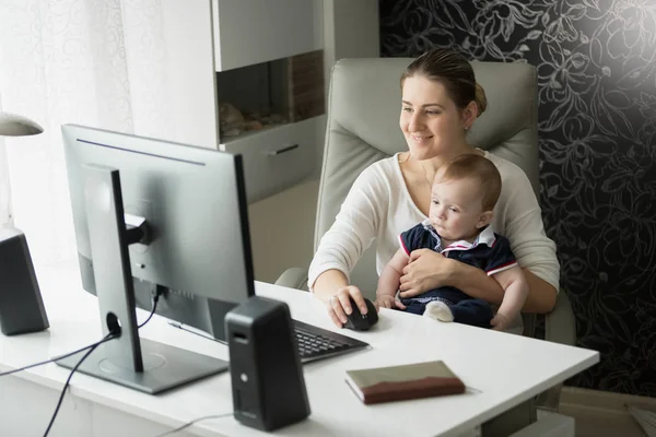 Mamma med hennes baby son i office med hjälp av dator — Stockfoto