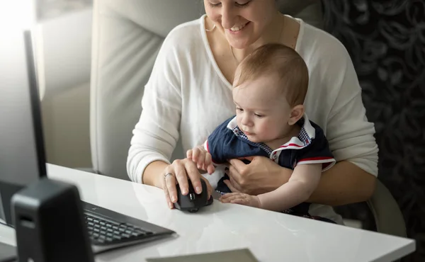 Söt baby pojke sitter i mödrar knä och leker med datorn m — Stockfoto