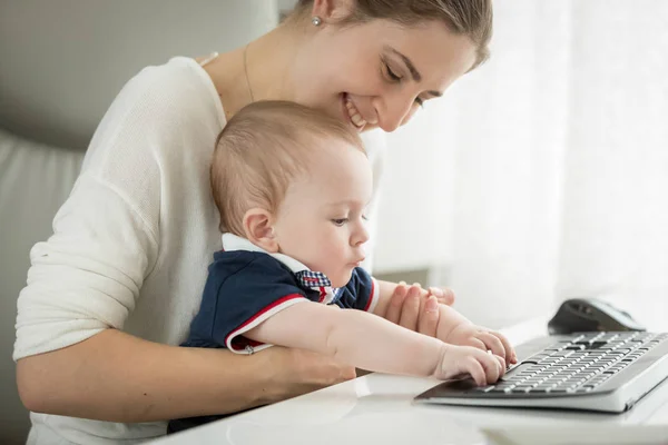 Söt baby sitter i mödrar knä och att skriva på tangentbordet — Stockfoto