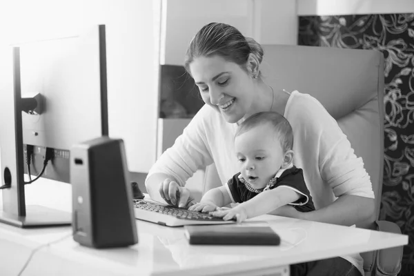 Fekete-fehér portré fiatal anya vigyáz a baba és a munka — Stock Fotó