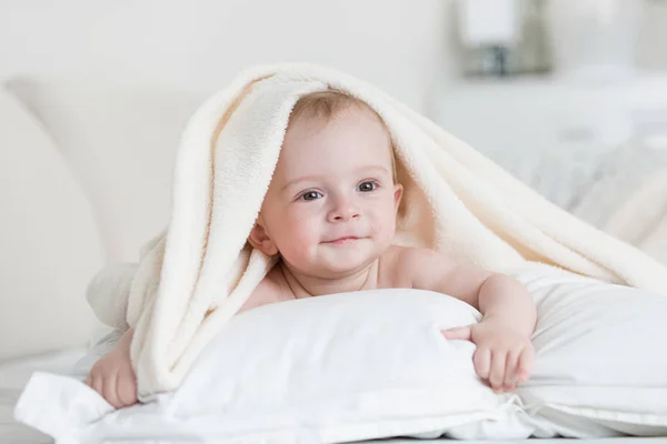 Cute baby boy lying under white blanket on bed — Stock Photo, Image