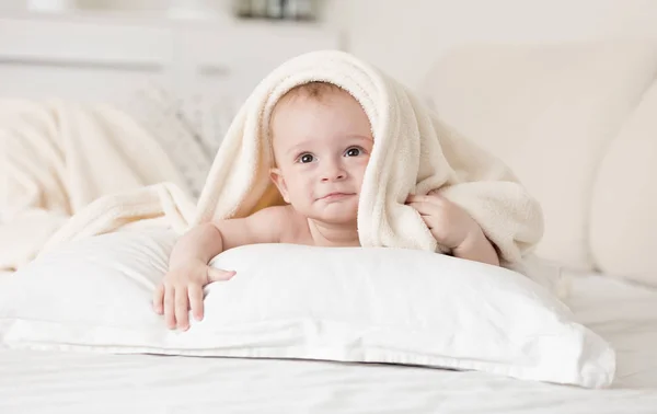 Söt baby pojke liggande på sängen under handduk efter badet — Stockfoto