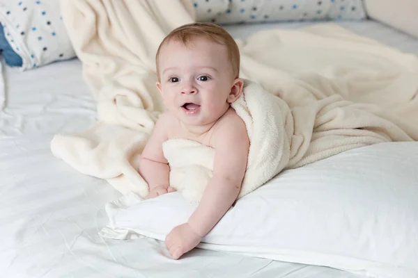 Alegre bebé niño acostado en una almohada grande debajo de una manta blanca — Foto de Stock