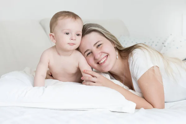 Happy smiling baby boy and mother lying on pillow and looking at