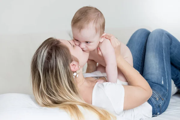 Feliz joven madre sentada en la cama y sosteniendo su 9 meses b —  Fotos de Stock