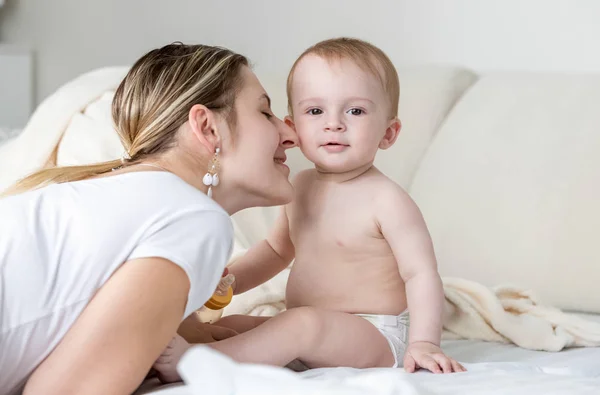 Gyönyörű fiatal anya csókolózás baba fiú arcát ágyon — Stock Fotó