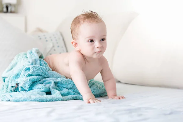 9 měsíců chlapeček v modrém ručníku na posteli s bílými listy — Stock fotografie