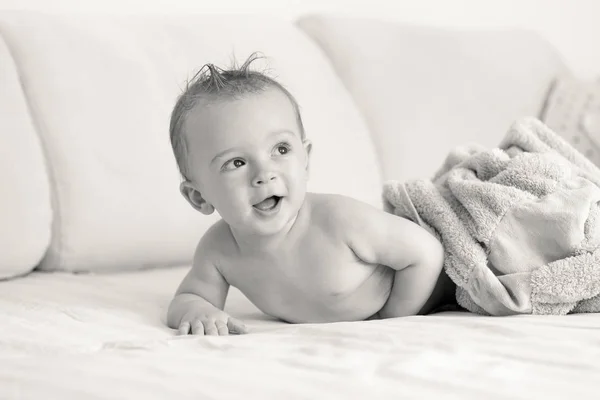 Black and white portrait of baby boy lying under blanket on sofa