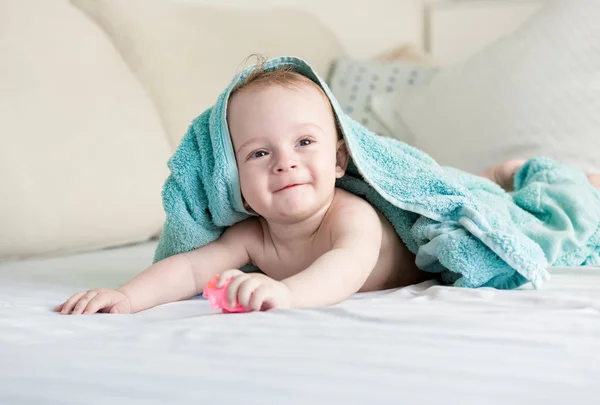Szczęśliwy uśmiechający się dziecko pod niebieski ręcznik czołgał się na łóżku z s biały — Zdjęcie stockowe