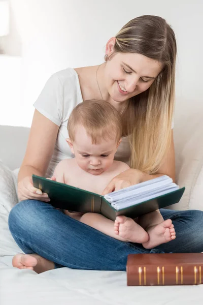 Mãe e seu menino de 9 meses sentado no sofá e lendo — Fotografia de Stock