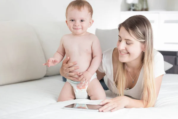 Sonriente madre y bebé niño usando tableta digital en la cama —  Fotos de Stock