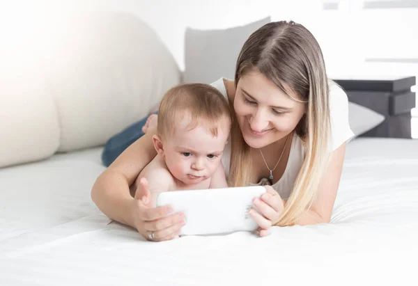 Bela jovem mãe deitada com seu bebê na cama e usando tabl — Fotografia de Stock