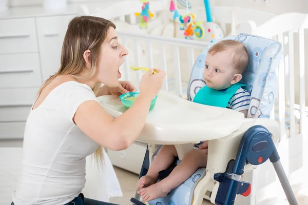 Mujer sonriente alimentando a su bebé en silla alta en la sala de estar —  Fotos de Stock