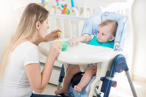 Mãe alimentando seu bebê em cadeira alta na sala de estar — Fotografia de Stock