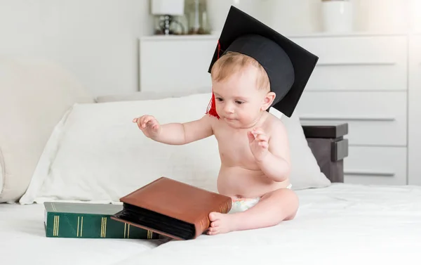 10 månader gammal pojke i mortarboard hatt sitter med stora böcker — Stockfoto