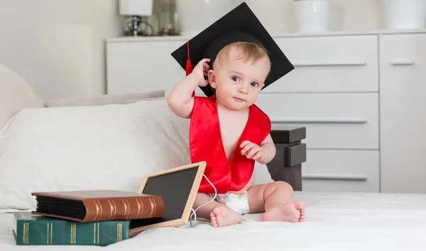 Divertente bambino ragazzo in nero graduazione cap holding libro — Foto Stock