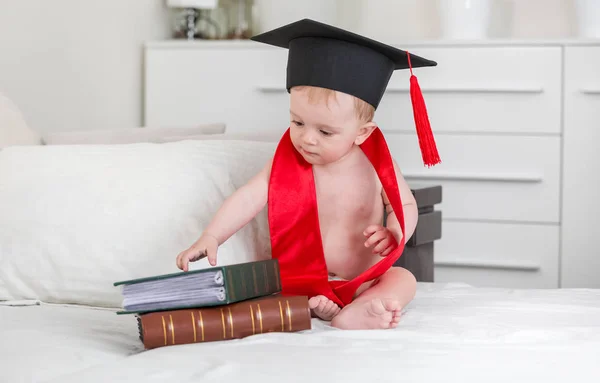 Förtjusande baby boy i examen cap och röd krage sitter på vara — Stockfoto