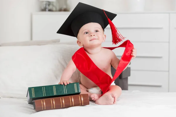 Portrait of cute baby boy in graduation sitting with books on so — Stock Photo, Image