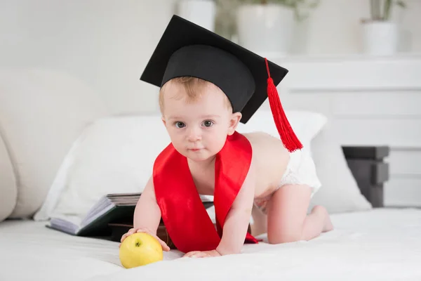 Bebé prodigio en gorra de graduación alcanzando la manzana — Foto de Stock