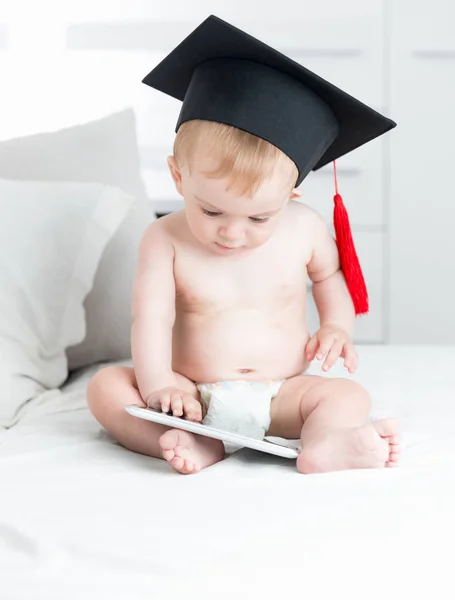 Adorabile bambino che indossa il berretto di laurea e utilizza la tabella digitale — Foto Stock