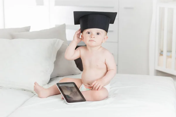 Portrait of funny baby boy in graduation cap using digital table — Stock Photo, Image