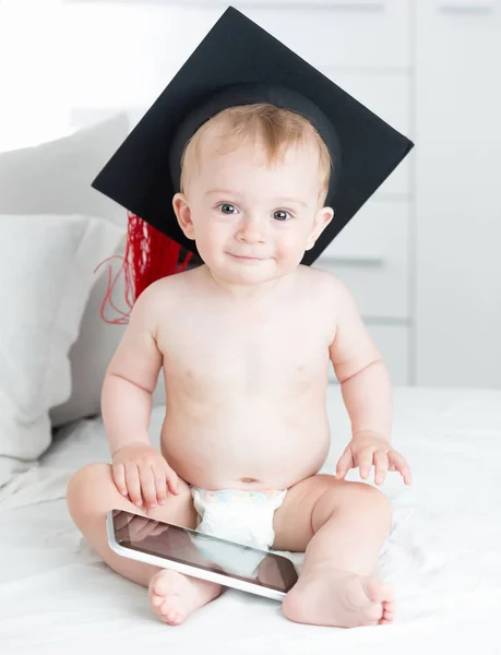 Porträtt av söt leende baby i examen cap sitter på soffa — Stockfoto