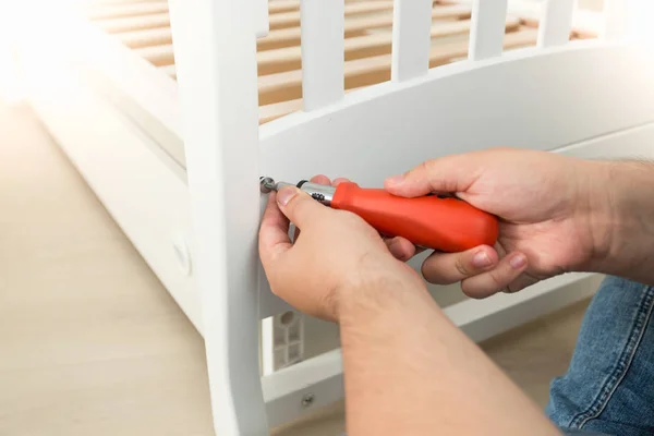 Fechar o handyman apertando os parafusos na cama de madeira branca — Fotografia de Stock