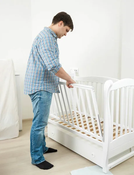 Knappe man in spijkerbroek en shirt montage babybed — Stockfoto