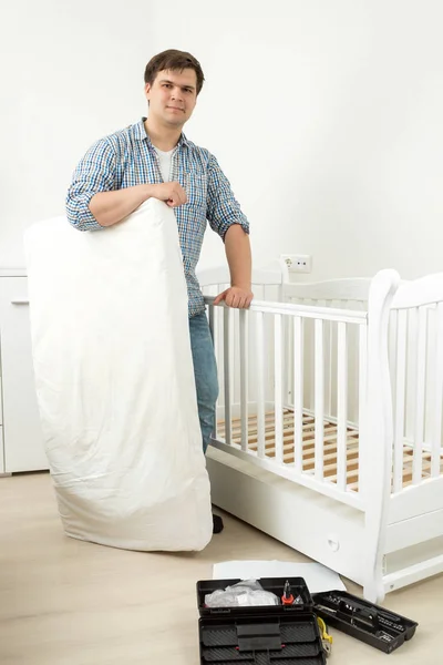 Glimlachende man die met matras bij gedemonteerde babybed — Stockfoto