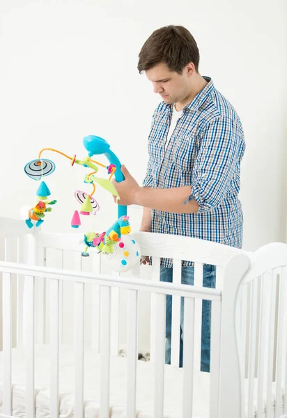 Молодой человек прикрепляет игрушечную карусель к детской кроватке — стоковое фото