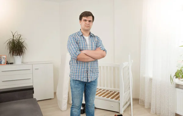 Young handsome man standing at disassembled baby crib — Stock Photo, Image