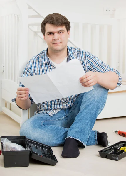 Puzzled man reading assembly instructions to baby\'s cot