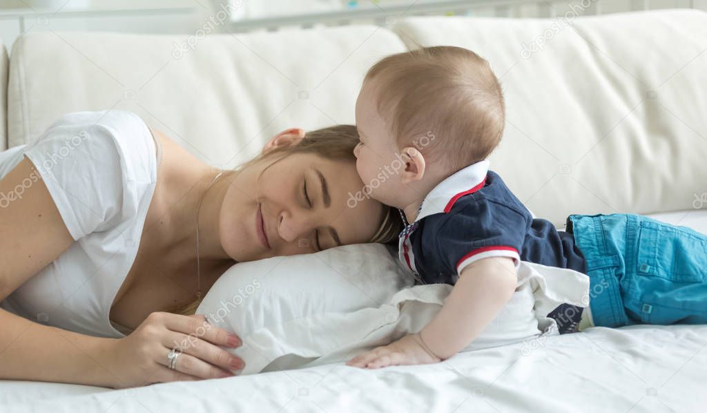 Portrait of cute baby boy lying with young mother on bed