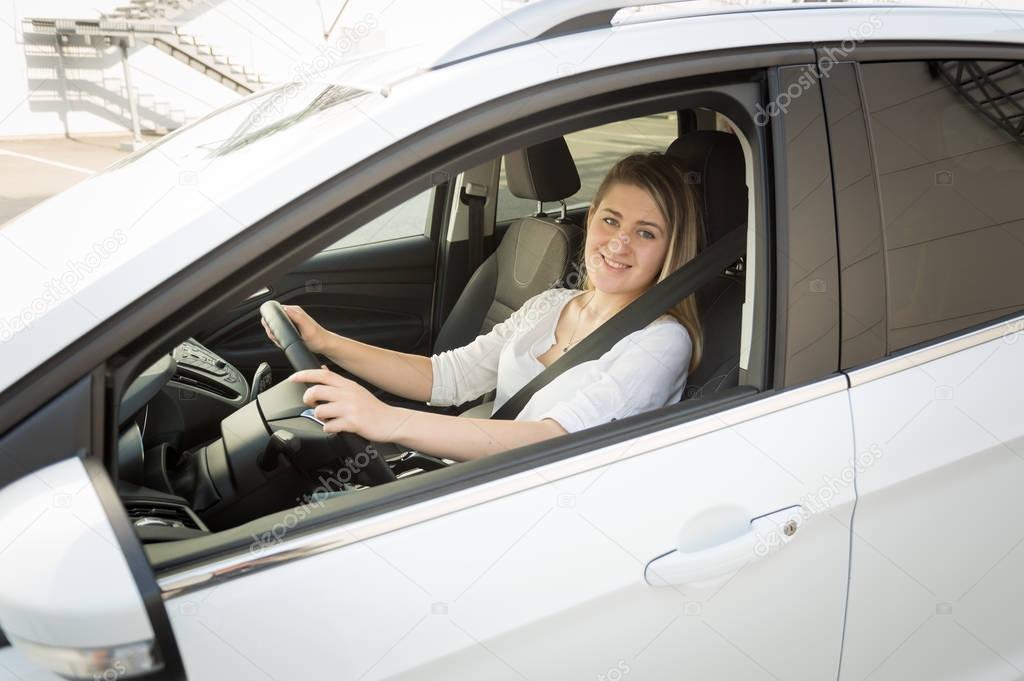 Smiling blonde woman in white shirt driving car