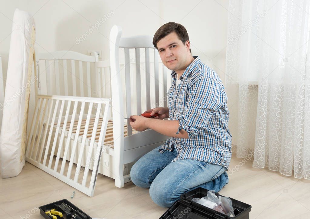 Young man sitting on floor and repairing child's bed
