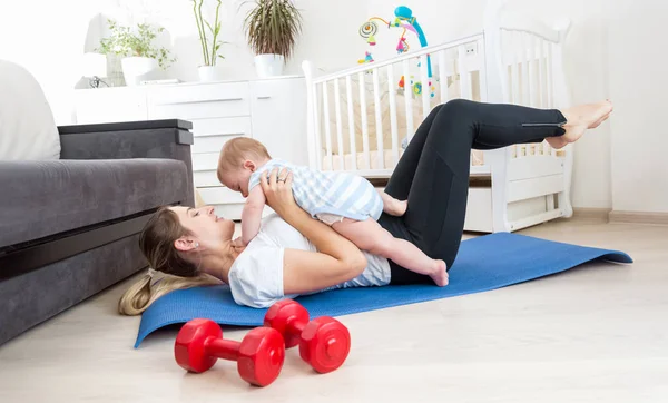 Madre feliz haciendo ejercicio en casa y divirtiéndose con su bebé — Foto de Stock