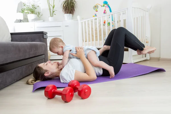 Madre feliz haciendo ejercicio en casa y divirtiéndose con su bebé — Foto de Stock