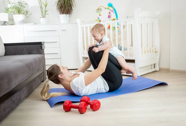 Joven madre sosteniendo al bebé y practicando yoga — Foto de Stock