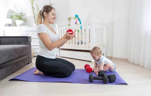 Mutter mit ihrem kleinen Sohn sitzt zu Hause auf Fitnessmatte und trainiert — Stockfoto